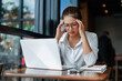 © Crystal - Young Asian businesswoman suffering from headache while working on laptop in cafe, touching temples with fingers, tired and exhausted