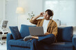 © Crystal - Asian freelancer listening to music with headphones while working on laptop, sitting comfortably on sofa in home office