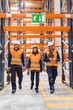 © Koldo_Studio - Logistics workers wearing safety vests and helmets are walking through a warehouse, using handheld devices to check inventory and manage goods