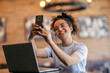 © Dusan Petkovic - Portrait of cheerful multicultural female remote worker sitting in cafe and taking selfies.