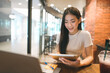 © dodotone - Young adult asian business woman using digital tablet and laptop freelancer digital nomad remote work at coffee cafe