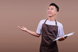 © Gatot - Happy Young Barista Man Holding Clipboard While Presenting To The Left Side
