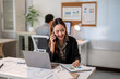 © Apichat - A woman is talking on her cell phone while sitting at a desk with a laptop