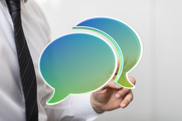Poster - Image depicts a businessman's hand holding two transparent speech bubbles, symbolizing communication and dialogue.