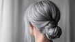 © Suphawan - Mature woman's head with long gray hair tied in a bun, soft background highlighting elegance and simplicity.
