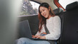 © Oil And Den - A smiling young woman is sitting in a car with a laptop on her lap