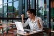 © Crystal - Young Asian freelancer raising arms in excitement while looking at laptop screen, celebrating successful project or good news in modern cafe