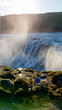 © Fokke Baarssen - At the Dettifoss waterfall in Iceland, two people stand in awe, gazing at the majestic water cascade. Mist rises from the roaring falls, illuminating the rocky terrain in golden light during sunset.