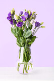 Vase with eustoma flowers on table near lilac wall