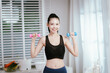 © Natthawadee - A focused young woman in a sports bra is exercising with light dumbbells, dedicated to her home fitness routine.