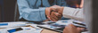 © crizzystudio - Business people shaking hands after discussing financial charts and graphs late at night