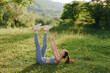 © SHOTPRIME STUDIO - Young woman exercising outdoors in the summer, practicing leg raises in a lush green field, showcasing healthy lifestyle and fitness routine