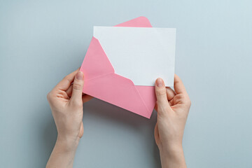 Wall Mural - Woman holding envelope with blank invitation card on grey background, top view. Space for design