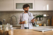© Stockphotodirectors - A man stands in a contemporary kitchen, sipping coffee from a mug, while looking at his smartphone with a content smile during a relaxed morning.