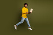 © deagreez - Young man in casual attire enthusiastically using a laptop while leaping against a moss green background