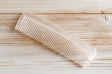 Fine-toothed plastic comb resting on a wooden surface for hair styling and grooming purposes