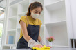 © Kield KD - A woman is cleaning a counter with a yellow cloth and a spray bottle. The counter is made of granite and is in a kitchen