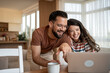 © Migma_Agency - Happy couple laughing and browsing internet on laptop at home