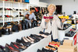 © JackF - Senior woman standing in salesroom of shoeshop and choosing moccasins. woman making purchases in background.
