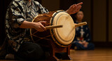Person in kimono playing taiko drum with wooden sticks on a wooden stand in a dimly lit room