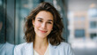 © Ольга Ничипорчук - Smiling brunette woman in blazer leaning against a glass wall in the city, friendly expression, business-casual style, modern urban workplace vibe brunette woman, business casual,