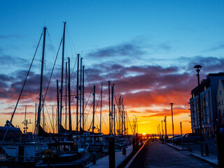Wall Mural - A sun rise over a marina with silhouettes of masts of many boats and yachts docked. Teal and orange color scheme. Calm and relaxing mood. Port of Galway, Ireland.