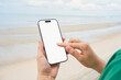 © Nuttima - Hand holding a smartphone with a blank screen, on the sea and sandy beach background. Summer vacation concept.