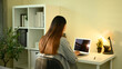 © saltdium - Rear view of a woman working at a home office desk with a laptop, plant, and cozy lighting setup