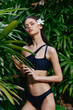 © SHOTPRIME STUDIO - Tropical beauty in black bikini with flower in hair posing among lush green plants