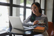 © Parichat - Smiling young woman using laptop and drinking coffee sitting in cafe