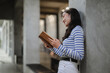 © Parichat - Young woman reading a book leaning against a wall
