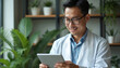 © Viktor - Asian doctor wearing lab coat examines digital tablet. Male medical expert, smiles, working at clinic. Professional medic with eyeglasses in hospital, medical research and tech.