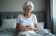 © Viktor - Unhappy elderly woman sitting bed, feeling strong belly ache. Senior lady, suffering stomach pain, indigestion. Abdominal disease, healthcare concept. Health problems with abdomen.