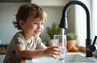 © Viktor - Smiling child draws water from kitchen faucet into glass. Kid enjoys clean water in home. Concept availability, safety of clean water, childhood hydration.