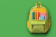 © Andrey - Colorful backpack filled with school supplies on vibrant green background promoting back to school sale offers