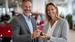 © Maksym - Happy salesman handing over key fob to smiling woman beside her new red car, banner with dealership logo in the background, bright celebratory setting