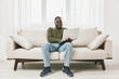 © SHOTPRIME STUDIO - Smiling young Black man working on a laptop in a cozy living room, wearing casual clothing, with soft lighting and a neutral color palette