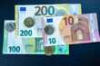 © Alex Malt - Euro banknotes (10, 100, 200) and coins (1, 2 euros and cents) arranged on a dark surface.