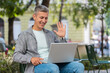 © Andrii Iemelianenko - Middle-aged man freelancer sitting in city street, looking at laptop camera, making video webcam conference call with friends, family or client, enjoying distant conversation. Mature guy waving hello.