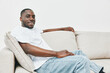 © SHOTPRIME STUDIO - Relaxed young African American man in casual white t shirt sitting on a light colored sofa, smiling, conveying comfort and ease