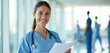 © miss irine - Smiling nurse portrait with document in modern hospital. Medical worker, confident friendly female doctor, healthcare pro looking to camera. Medicine, public service, health, wellness, help.