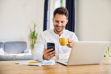 Smiling freelancer using mobile phone at home while working on laptop