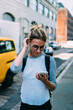 © BullRun - Young casually dressed female tourist walking on city street with smartphone using 4G connection,hipster girl browsing application on telephone for calling taxi making payment online while strolling