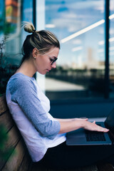 Wall Mural - pensive female student keyboarding on netbook searching tutorial while sitting outdoors on bench,hip