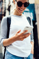 Wall Mural - Cropped image of cheerful hipster girl satisfied with good internet walking on street chatting via mobile phone,smiling female traveler strolling in town using navigation on smartphone checking route