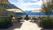 © visoot - Outdoor terrace with tables, chairs, and umbrellas overlooks scenic lake and mountains under bright sky