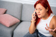 © Guillermo Spelucin - Redhead woman arguing on phone while sitting on sofa