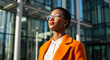 © budi - Confident businesswoman gazing upward, bathed in sunlight, stands before a modern glass building.