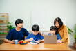 © laddawan - Homeschool Asian young little boy learning online and does homework by using computer and tablet with mother help, teach and encourage.