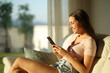 © Antonioguillem - Happy woman at home at sunset using mobile phone